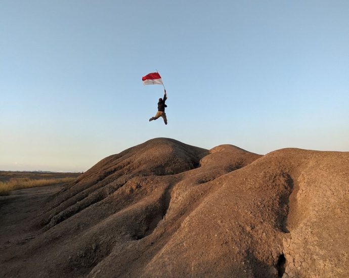 person with flag of indonesia jumping on barren rocks
