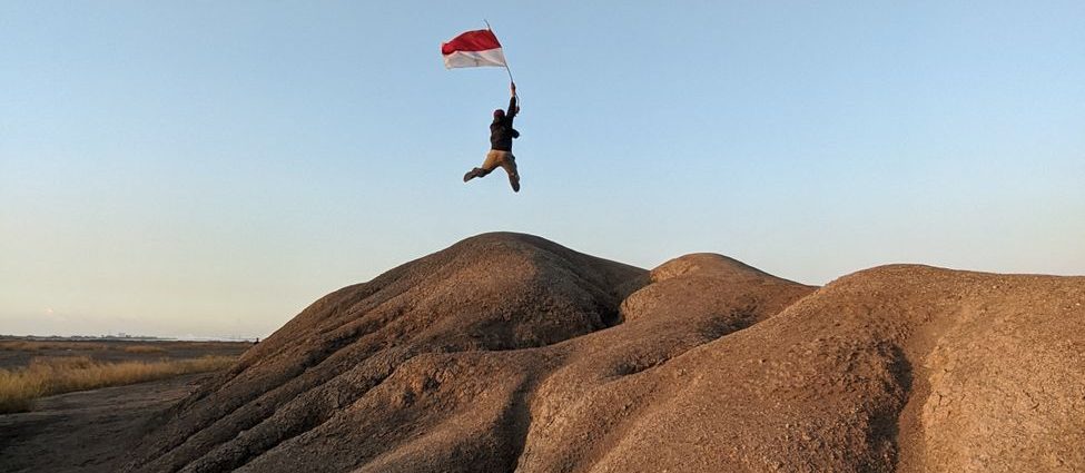 person with flag of indonesia jumping on barren rocks