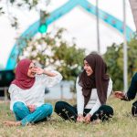 young muslim women laughing while resting on grass