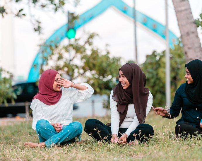 young muslim women laughing while resting on grass